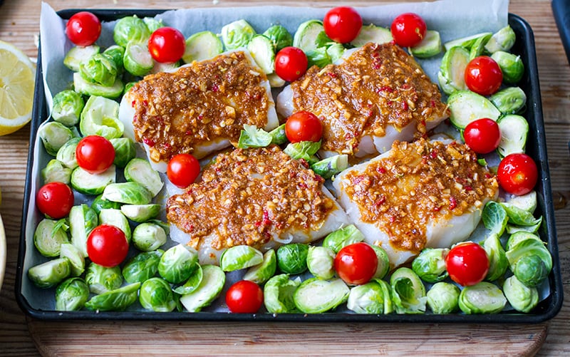 A tray with baked cod fillets, tomatoes and Brussel sprouts