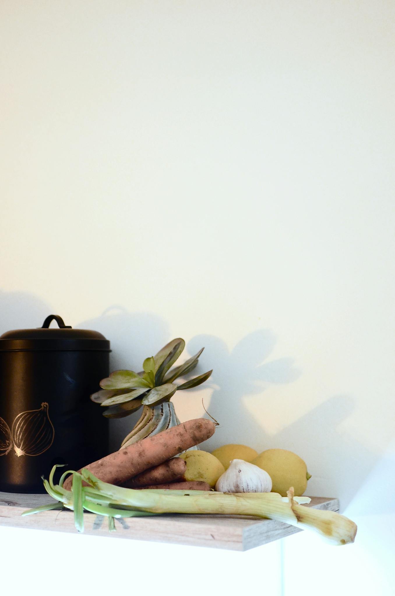 Arrangement of fresh vegetables and a cactus on a kitchen shelf, ideal for healthy living concepts.